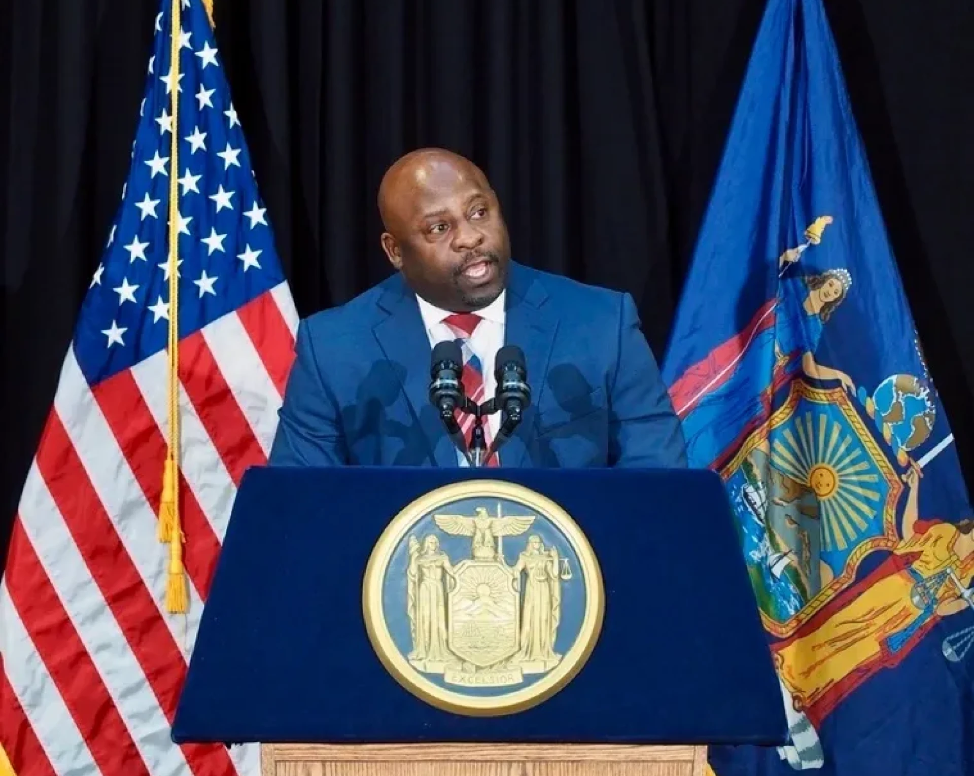 Man speaking at podium with two flags.